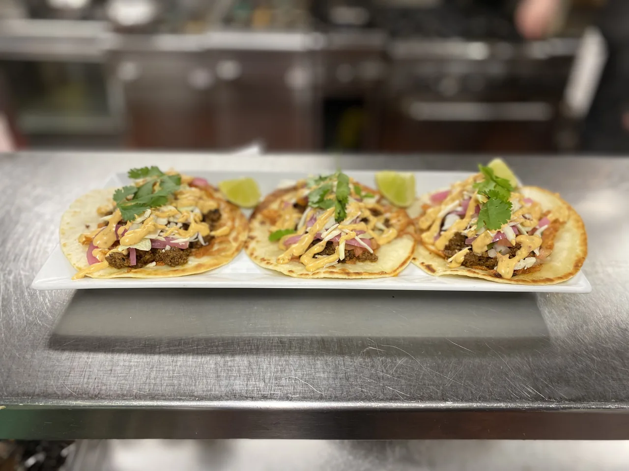 Three tacos lined up on the pass