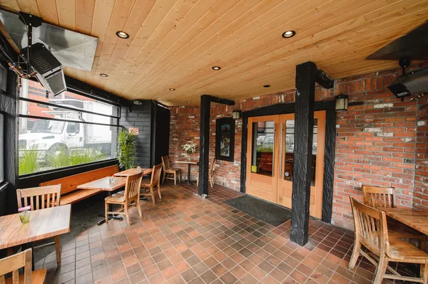The covered terrace by the entrance doors, with brick walls, a wood ceiling and patio heaters