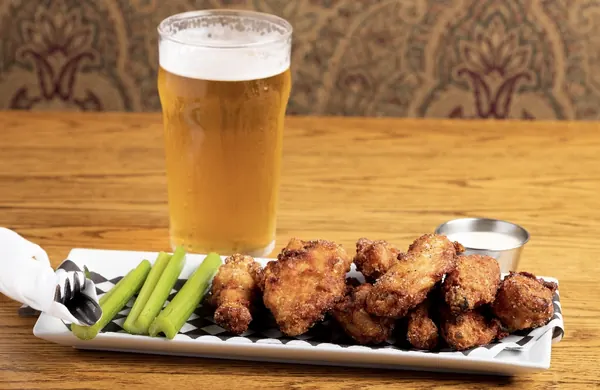 Chicken wings with celery and a cold lager on the bar